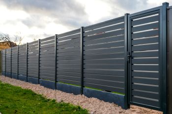 Modern dark gray metal privacy fence along a landscaped yard under cloudy sky