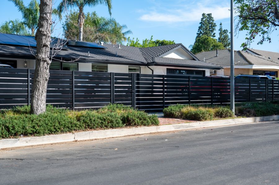 Black aluminum privacy fence along a suburban home with landscaped front yard and street frontage